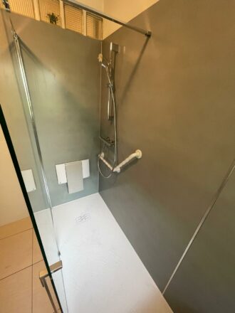 Douche PMR en un jour par Eau et Design : vue du siège, de la barre et la paroi de douche PMR